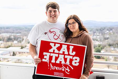 A freshman prospect and his mom hold the Jax State Bound sign on top of the library